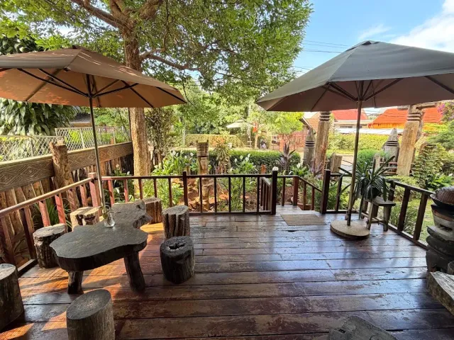 A wooden deck with two parasols, tree stump stools and a log table facing a garden