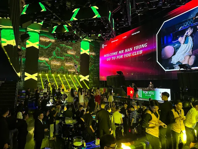 A crowded dance floor facing giant LED screens and green lighting in a club