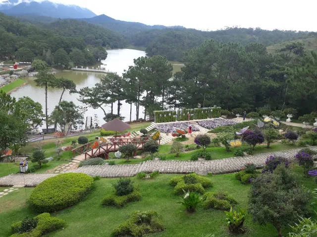 A manicured garden with clipped shrubs and paved paths, a lake and a pine forest behind