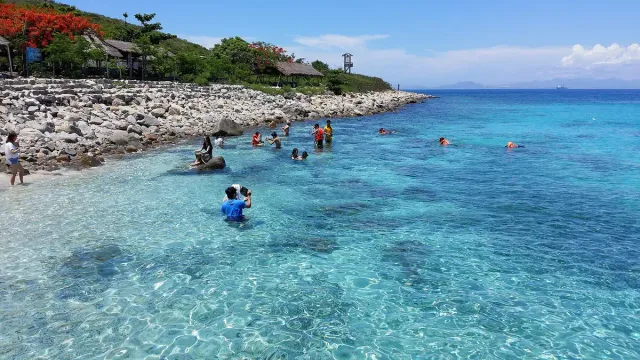 Clear turquoise water with swimmers and a pebble shore