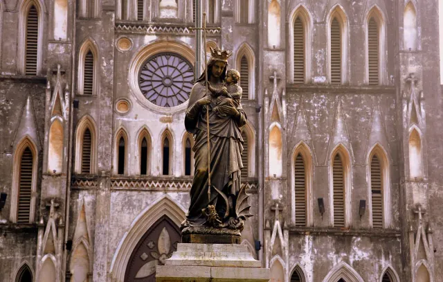 A statue of the Virgin on the grey stone gothic facade of a cathedral with a rose window