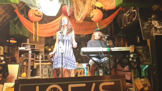 A singer and a keyboard player perform on a small stage decorated with orange pumpkins