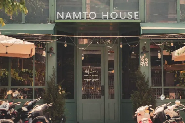 A green facade with string lights, glass doors and scooters parked along the pavement