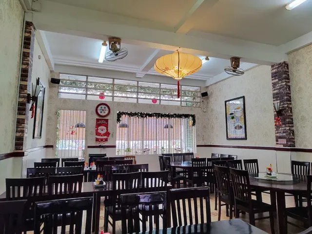 A dining hall with round tables, dark wooden chairs and a yellow paper lantern from the ceiling