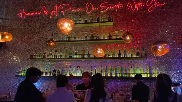 A mirror mosaic wall with lit bottle shelves, pink neon lettering and spherical light fixtures