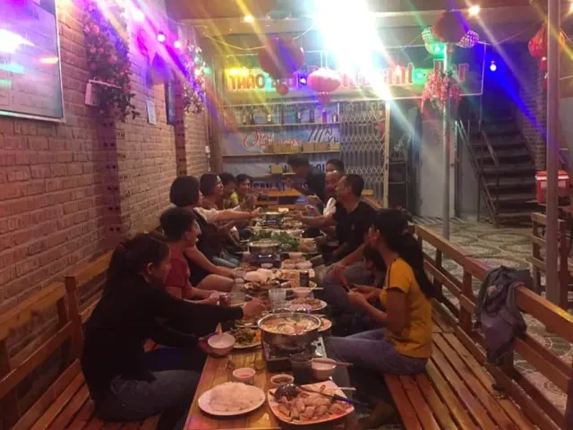 A group seated around a long table with hotpots, a brick wall and colored bulbs