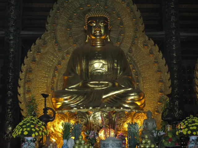 A large gilded Buddha statue inside a lit temple hall