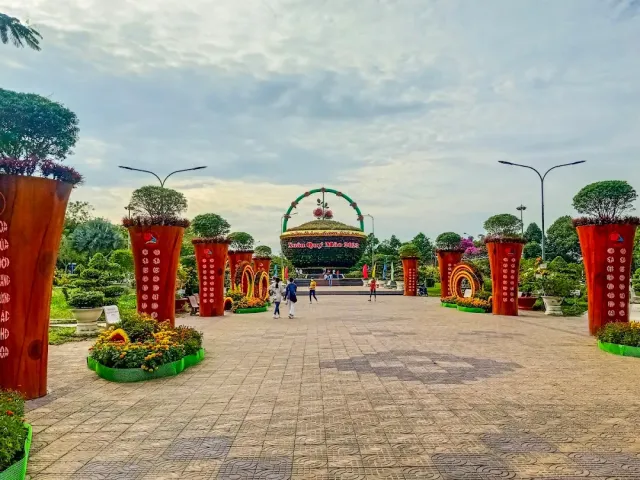 A wide paved promenade between tall planters and flower beds, an arched floral display in the middle