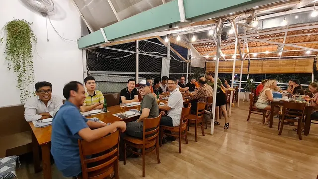 Diners at wooden tables on a covered rooftop terrace, with strings of lights in the evening