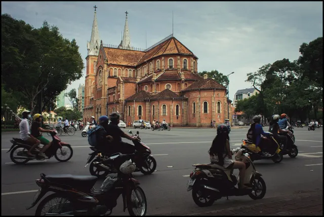 A red brick cathedral with twin spires, scooters passing in the square