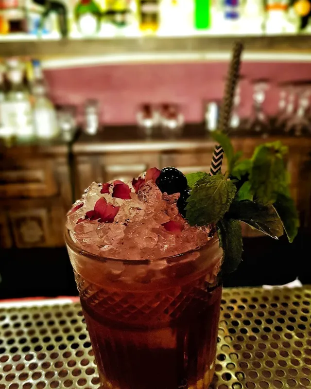 A cocktail in a ridged glass with crushed ice, petals, mint and a striped straw