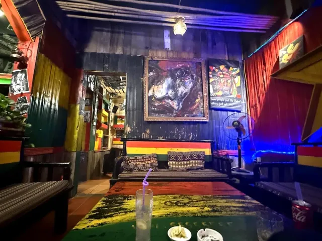 A wooden space painted in red yellow and green stripes with a framed painting and a low bench