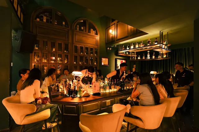 A warmly lit cocktail counter with pale armchairs and arched bottle cabinets