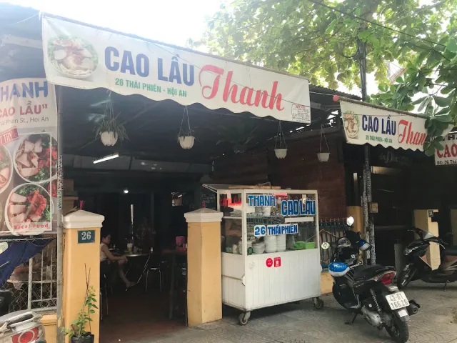 A street stall with white fabric signs, a serving cart and motorbikes parked to the side