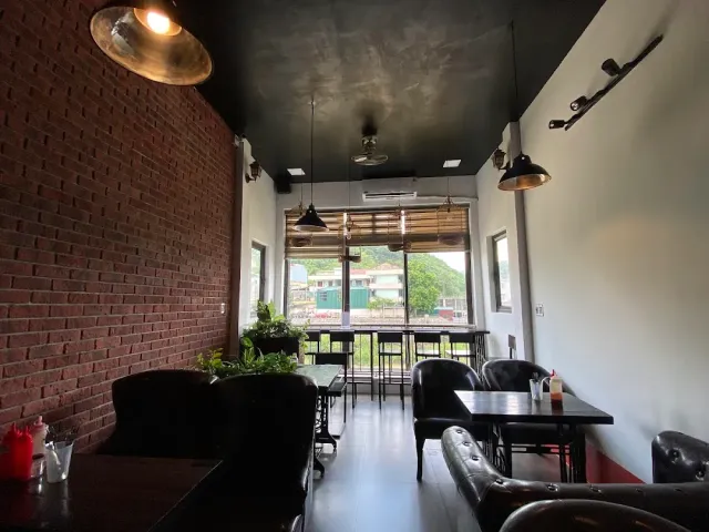 A narrow space with a red brick wall, industrial lamps, dark sofas and a window onto the hills