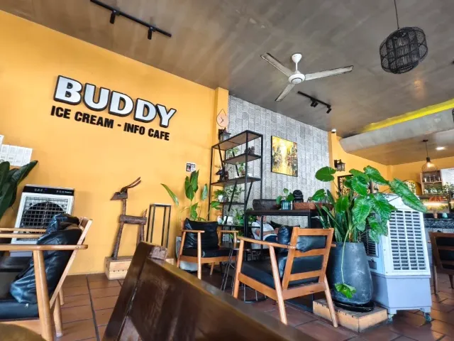 A space with a yellow wall and white letters, a bare concrete ceiling, wooden chairs and potted plants