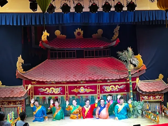 A stage shaped like a red roofed pavilion, six performers in colorful robes standing in a pool