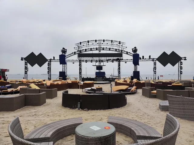 Wicker sofas and sunbeds on the sand facing a large stage by the sea