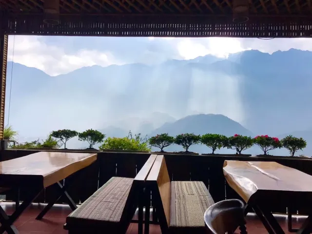 A terrace with wooden tables and benches, a row of planters on the railing and a misty mountain view