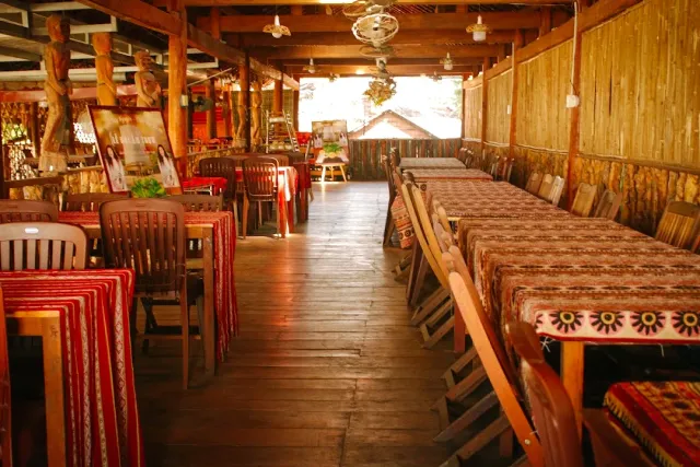 A long wooden hall with tables in patterned cloths, carved posts and bamboo walls