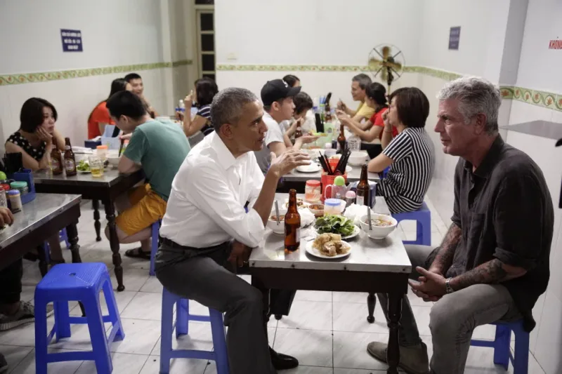 Barack Obama and Anthony Bourdain eating bun cha on blue plastic stools at the Hanoi restaurant
