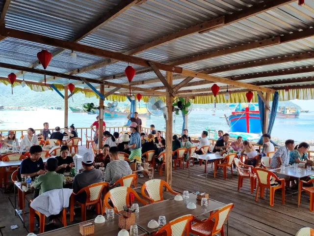 A covered wooden deck with red lanterns, plastic chairs and a view of the bay with fishing boats