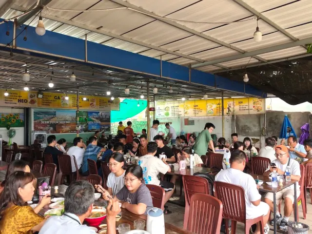 A bustling covered eatery with menu boards on the wall, red plastic chairs and diners
