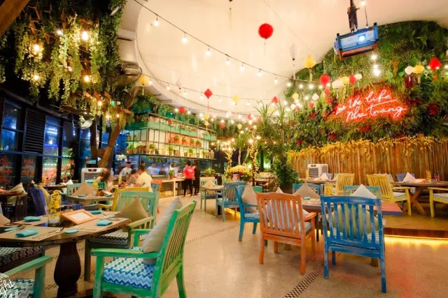 A colorful space with plant walls, hanging lanterns, a neon sign and turquoise and blue wooden chairs