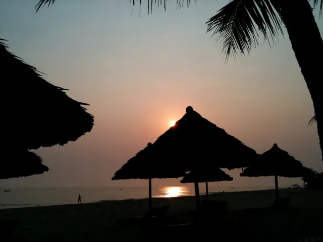 An orange sunrise across the sea, the silhouette of a thatched parasol in front