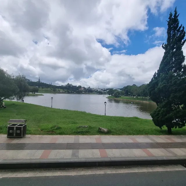 A calm lake surrounded by lawns and green trees, under partly cloudy skies