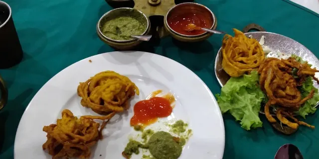 A plate of fried onion fritters with two sauces, on a green cloth beside a metal tray