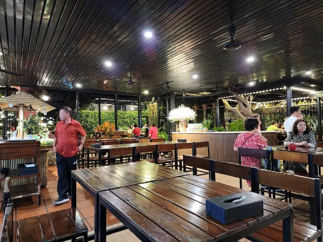 An open dining hall with wooden tables, a dark wooden ceiling and a sculpted tree in the center