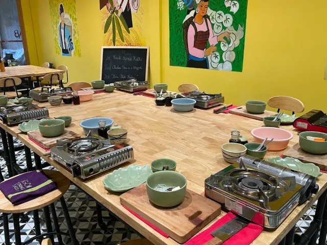 A long wooden table set with green bowls, portable burners and cutting boards