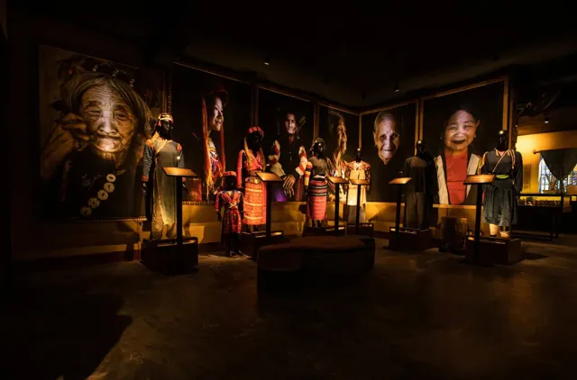 A dark exhibition hall with lit portraits and items of dress