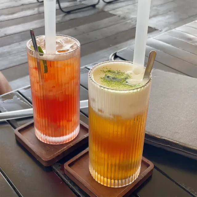 Two colorful drinks in ribbed glasses on wooden coasters, with white straws