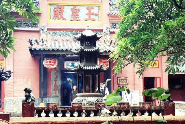 An ornate pink temple facade with tiled roofs and greenery