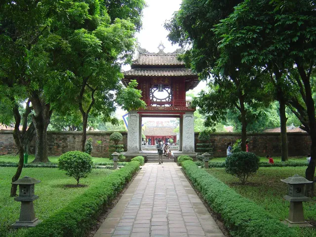 A paved path between lawn and trees leading to an old temple gate