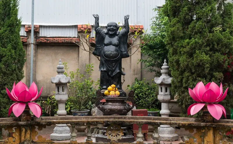 The laughing Buddha statue in the courtyard of Du Hang Pagoda in Hai Phong, between two pink lotus lanterns