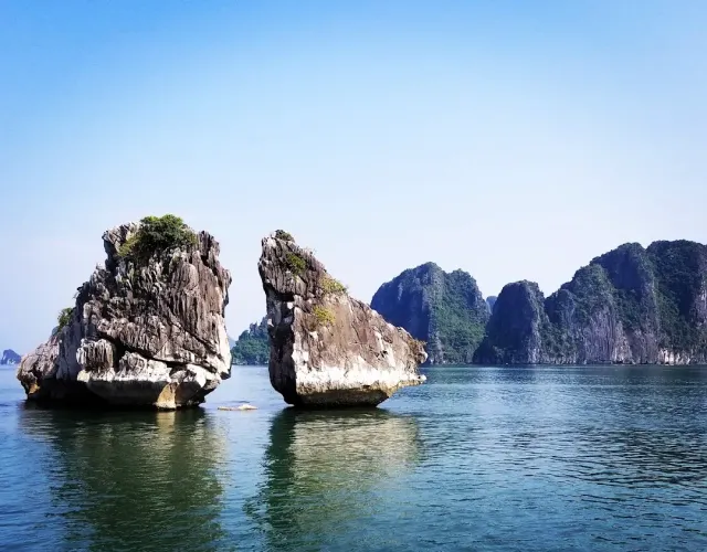 Two tall limestone rocks rising from greenish water, more karst islands behind