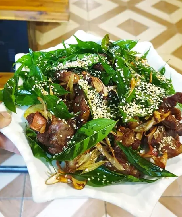 A white plate held in hand with stir fried meat pieces, green leaves and sesame