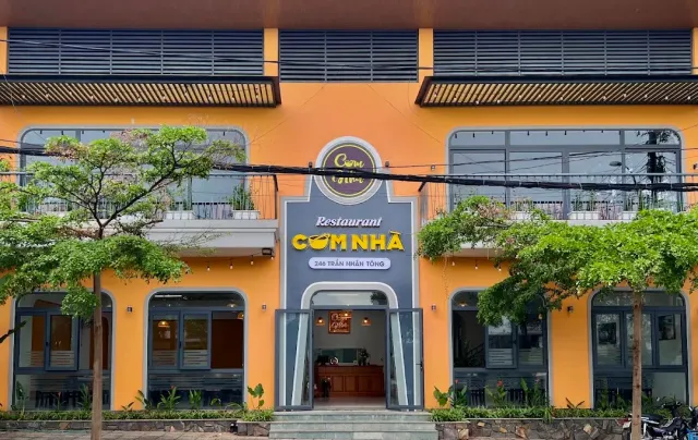 A two story orange building with a dark sign, arched windows and young trees in front