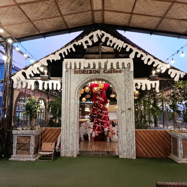 An entrance built like a snow covered house with string lights, a decorated tree inside and artificial grass