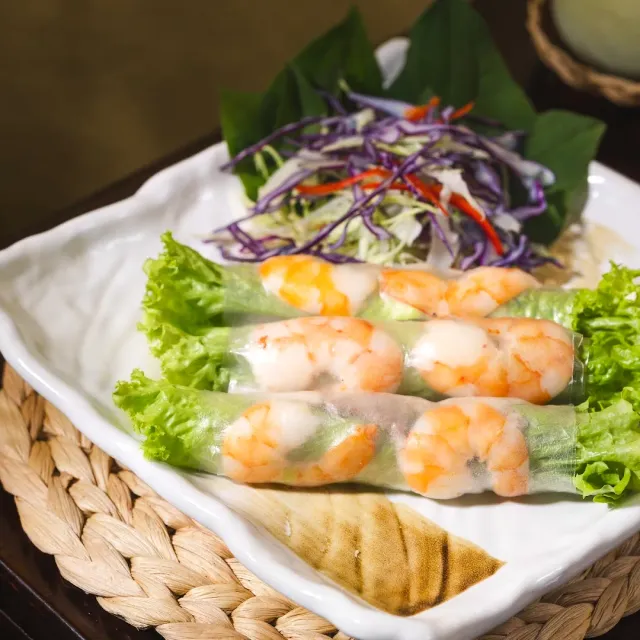 A white plate with three translucent rolls filled with shrimp, lettuce and shredded purple cabbage