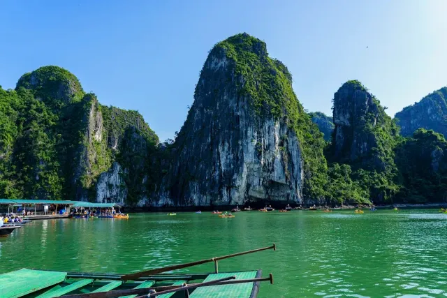 Limestone cliffs above green water, a floating pier and small kayaks near an opening in the cliff