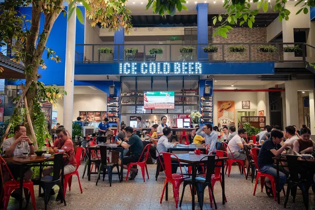 A covered courtyard with red chairs and full tables facing a beer tap counter