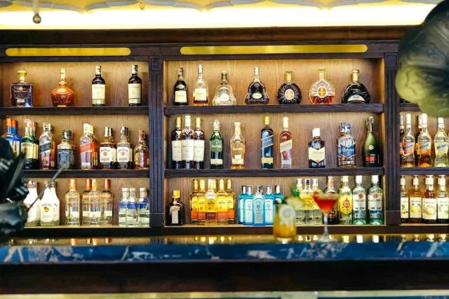 Wooden shelves full of liquor bottles, with a blurred cocktail in the foreground