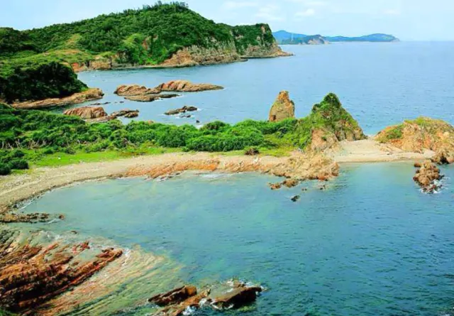 A view of a green headland with layered rock shelves, a shallow lagoon and open sea
