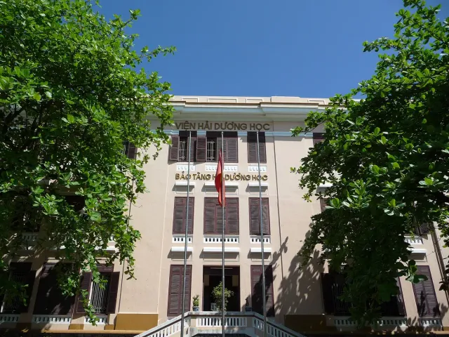 A yellow colonial institute building with tall trees in front