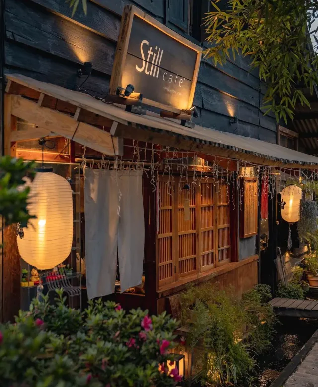 A dark wood facade at dusk with white paper lanterns and flowering shrubs