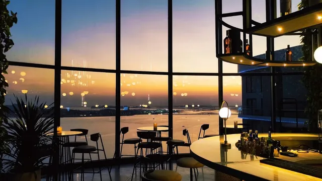 A curved bar counter facing tall windows overlooking a bay at sunset